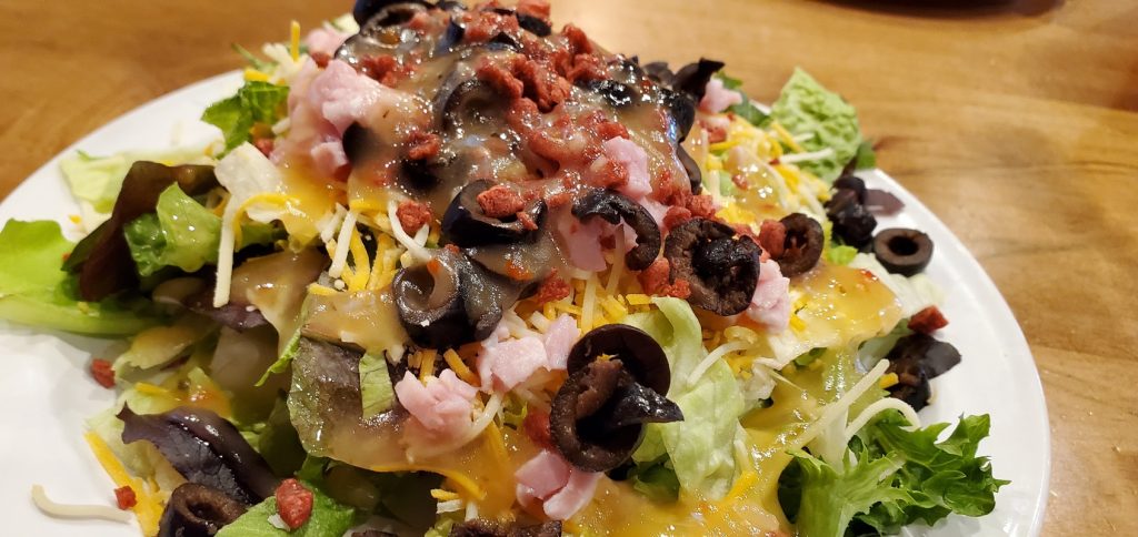 Salad with black olives, ham, bacon bits, cheese and Italian dressing